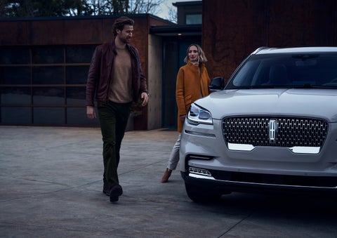 A man and a woman approaching a 2024 Lincoln Aviator® SUV, which illuminates certain lights when they are close | Dan Cummins Lincoln in Nicholasville KY