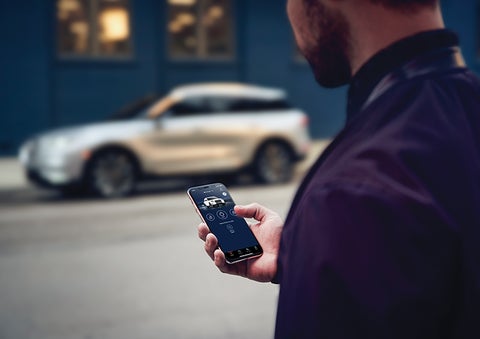 A person is shown interacting with a smartphone to connect to a Lincoln vehicle across the street. | Dan Cummins Lincoln in Nicholasville KY