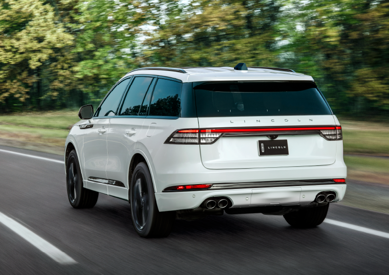 A white 2025 Lincoln Aviator® SUV is being driven away down a road lined with colorful trees. | Dan Cummins Lincoln in Nicholasville KY