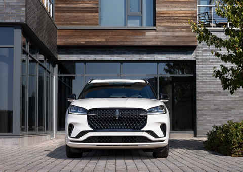 A white 2025 Lincoln Aviator® SUV is shown parked outside a modern building with gray brick and wood accents. | Dan Cummins Lincoln in Nicholasville KY