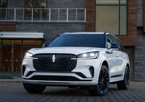 A white 2025 Lincoln Aviator® SUV is shown parked outside a modern building with gray brick and wood accents. | Dan Cummins Lincoln in Nicholasville KY