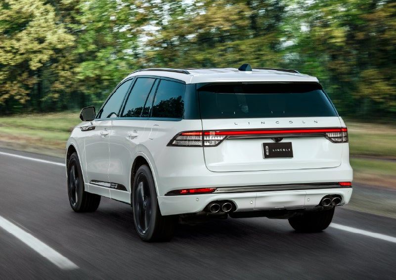 A white 2026 Lincoln Aviator® SUV is being driven away down a road lined with colorful trees. | Dan Cummins Lincoln in Nicholasville KY