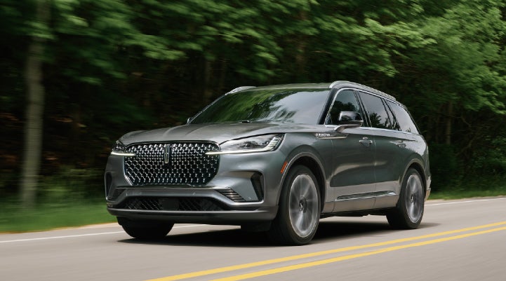 A 2027 Lincoln Aviator® SUV is being driven down a road lined with trees. | Dan Cummins Lincoln in Nicholasville KY